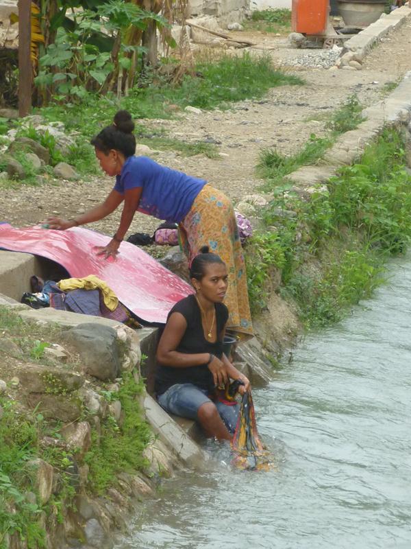 Family washing laundry in river in Maliana
